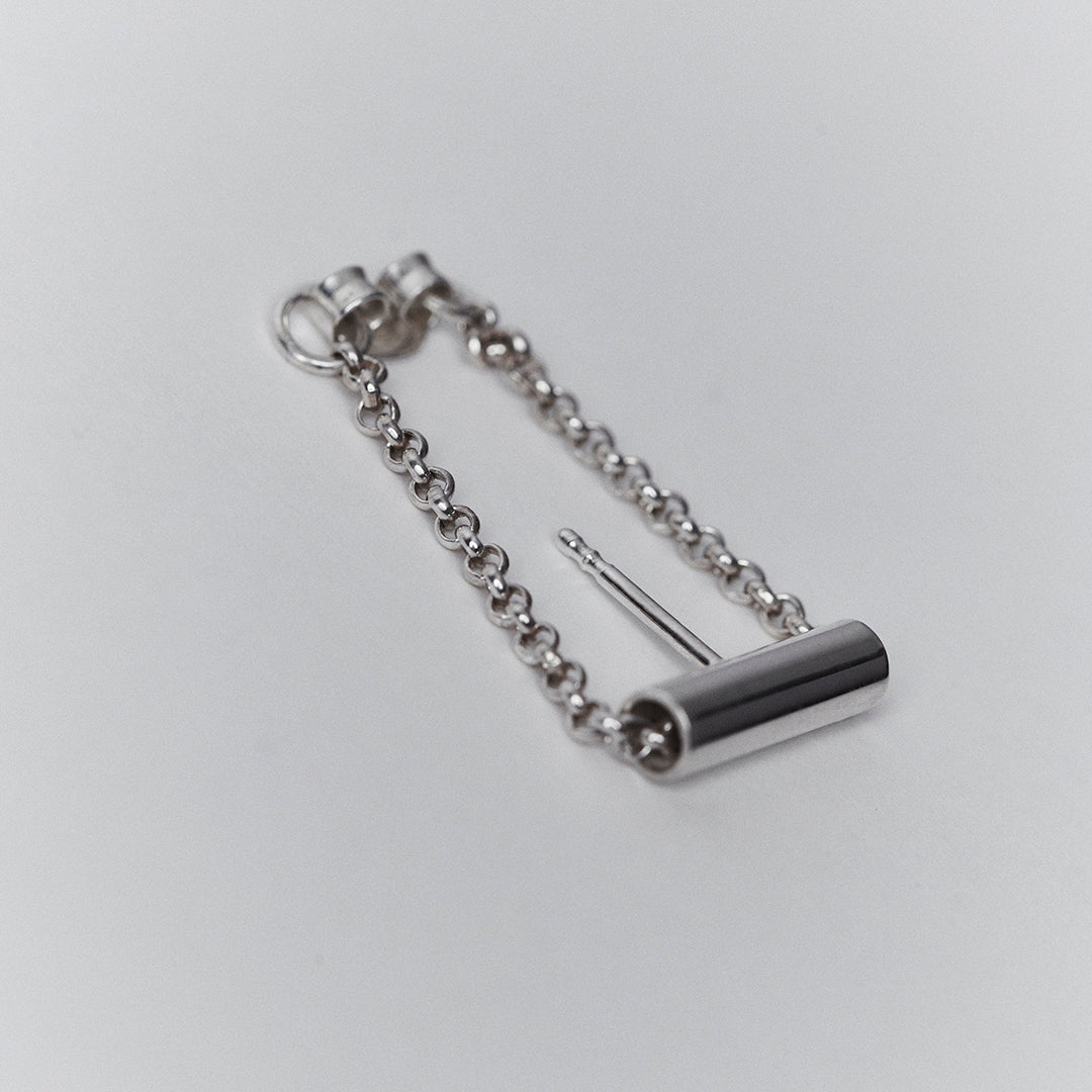 A silver earring with a chain running through a tube.
