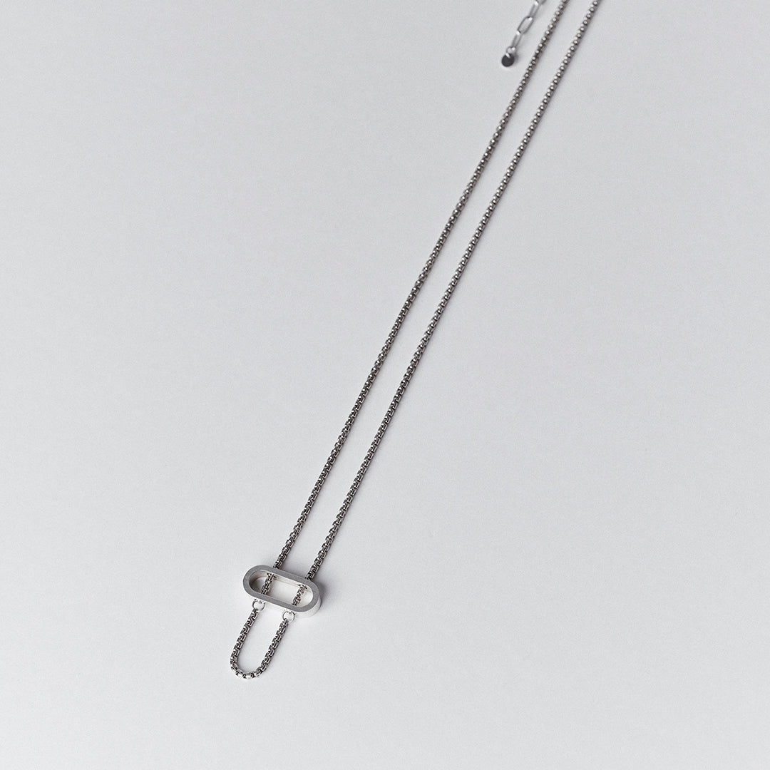 A silver necklace with a thick venetian chain threaded through an oval pendant.