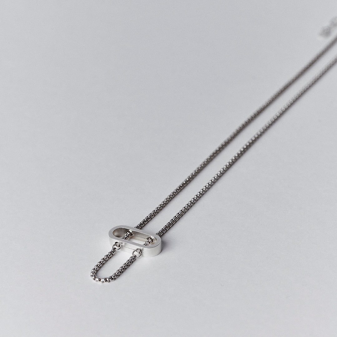 A silver necklace with a thick venetian chain threaded through an oval pendant.