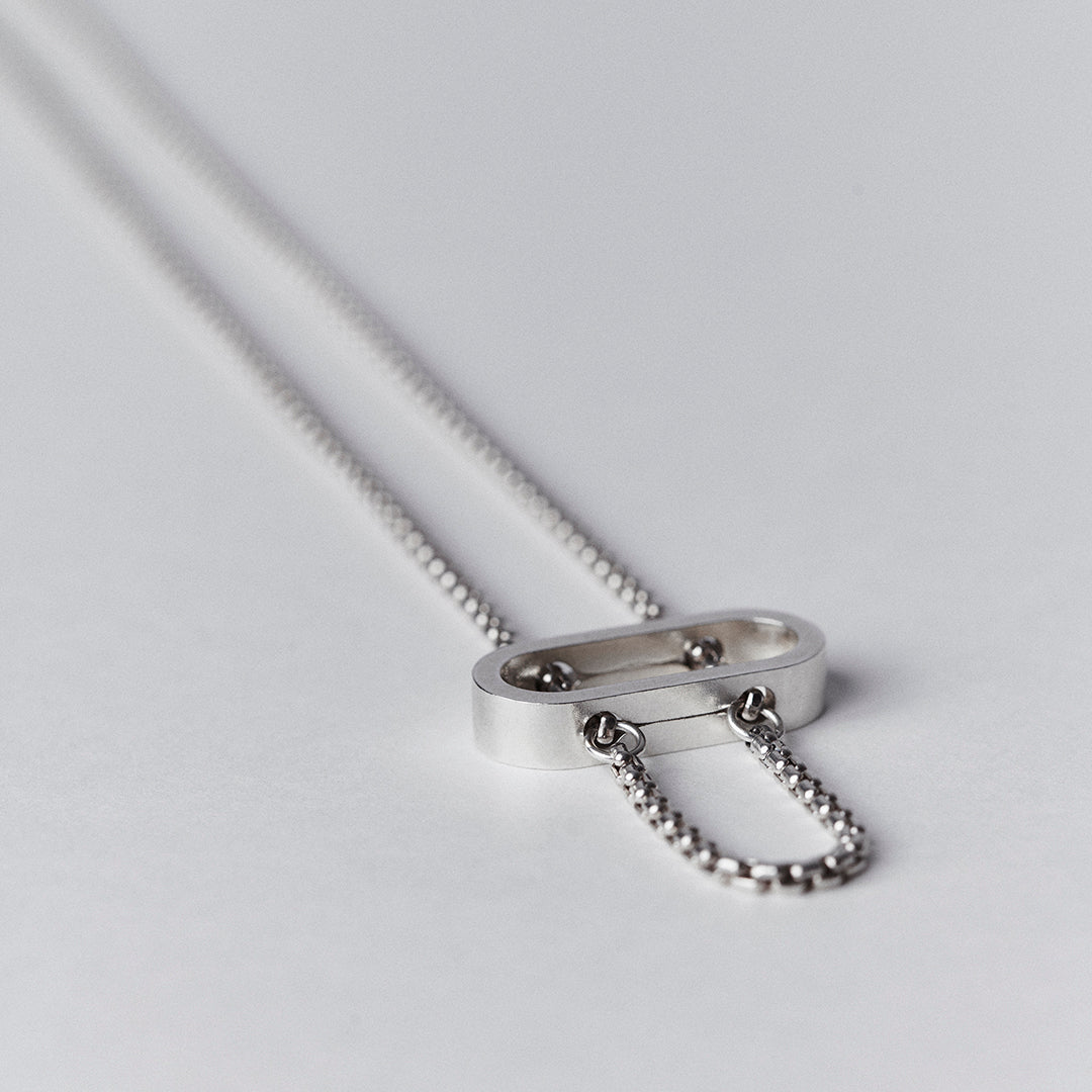 Silver necklace detail of a thick venetian chain threaded through an oval pendant.