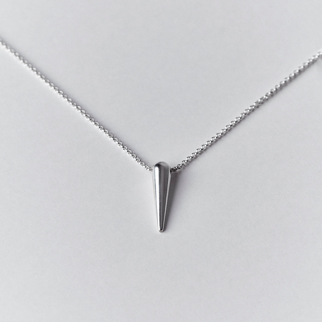 A woman's cheA silver chain and a silver spike shaped pendant.