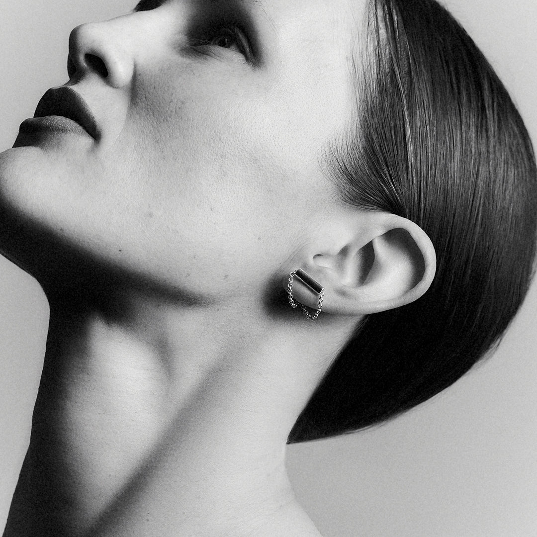 A woman's profile face shot, wearing a silver tube earring with a connected chain