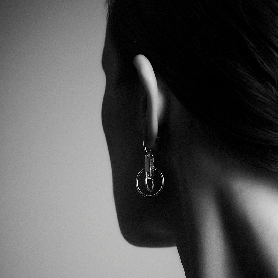 The back of a woman's head and ear, showing a silver earring with interlocking silver rings.