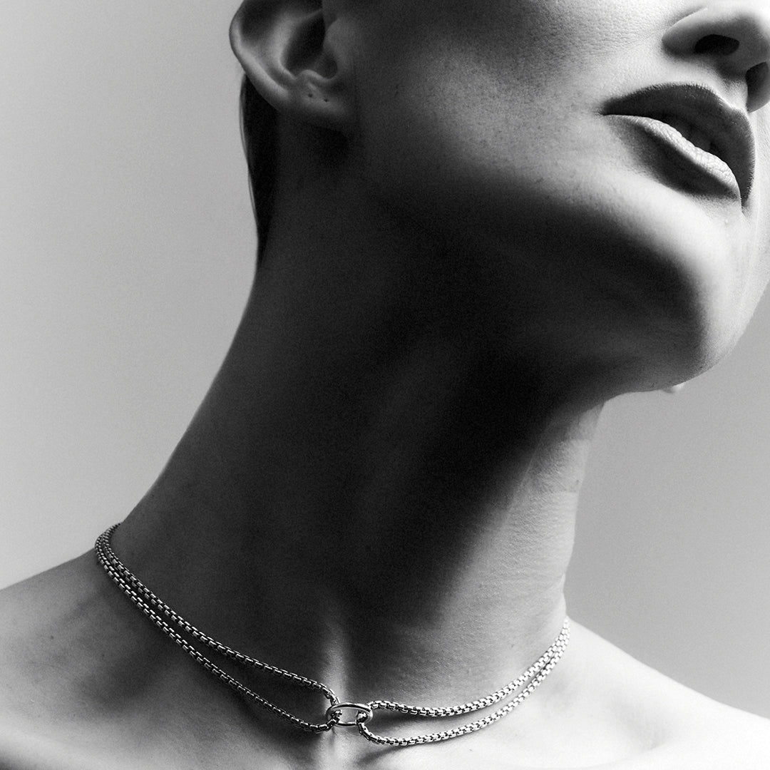Woman wearing a thick silver choker necklace with a double venetian chain and a central ring.