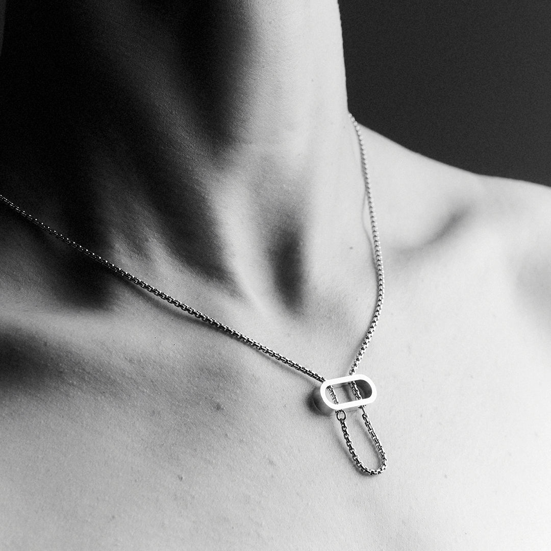 Woman's's chest wearing a silver necklace with an oval pendant and a thick venetian chain.