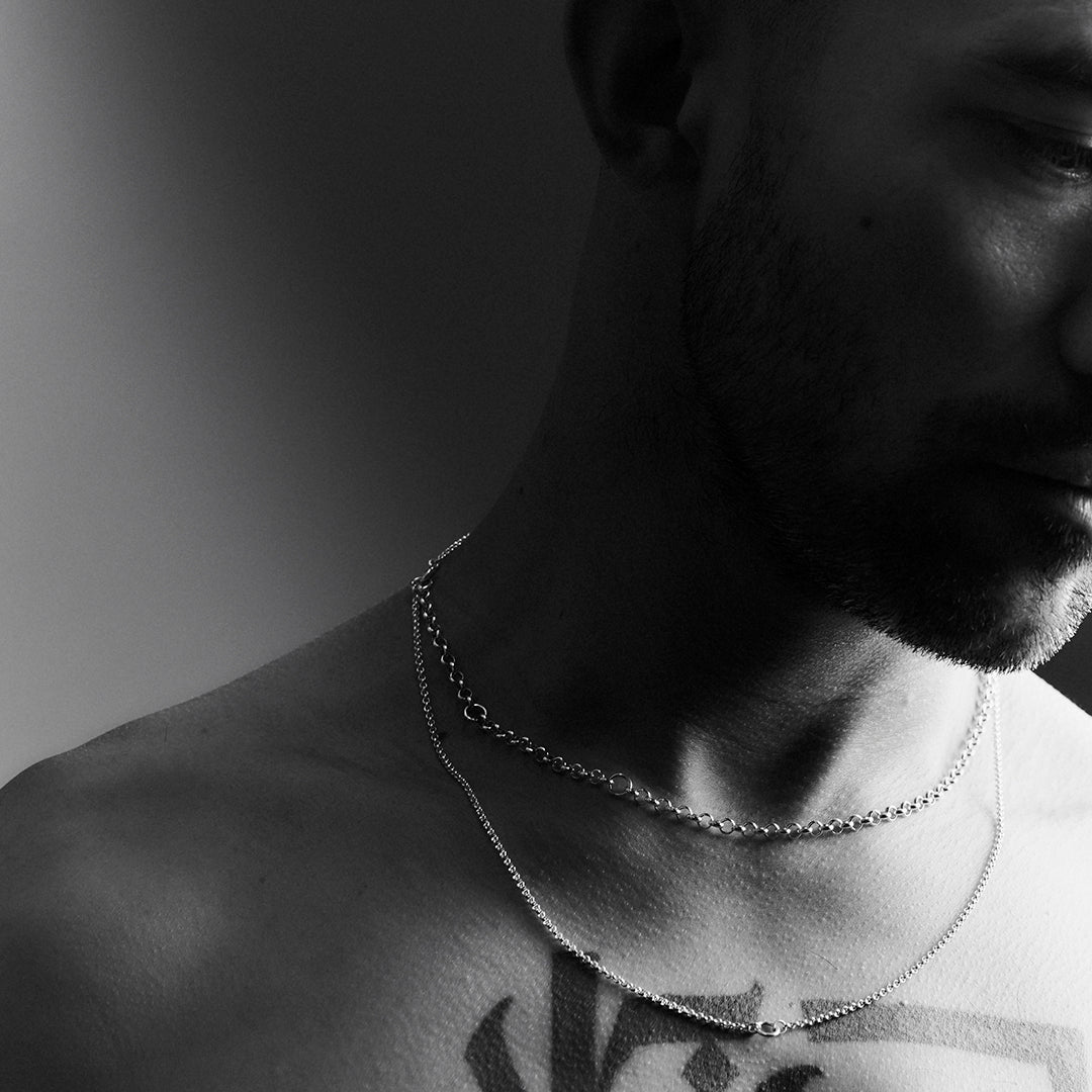 A man's face and neck wearing a double layered silver necklace.