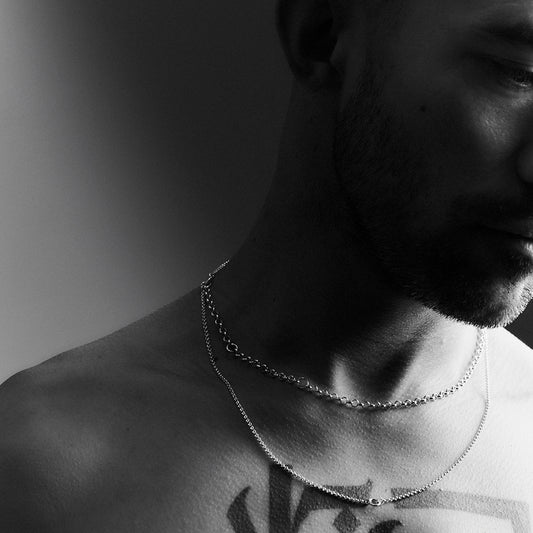 A man's face and neck wearing a double layered silver necklace.