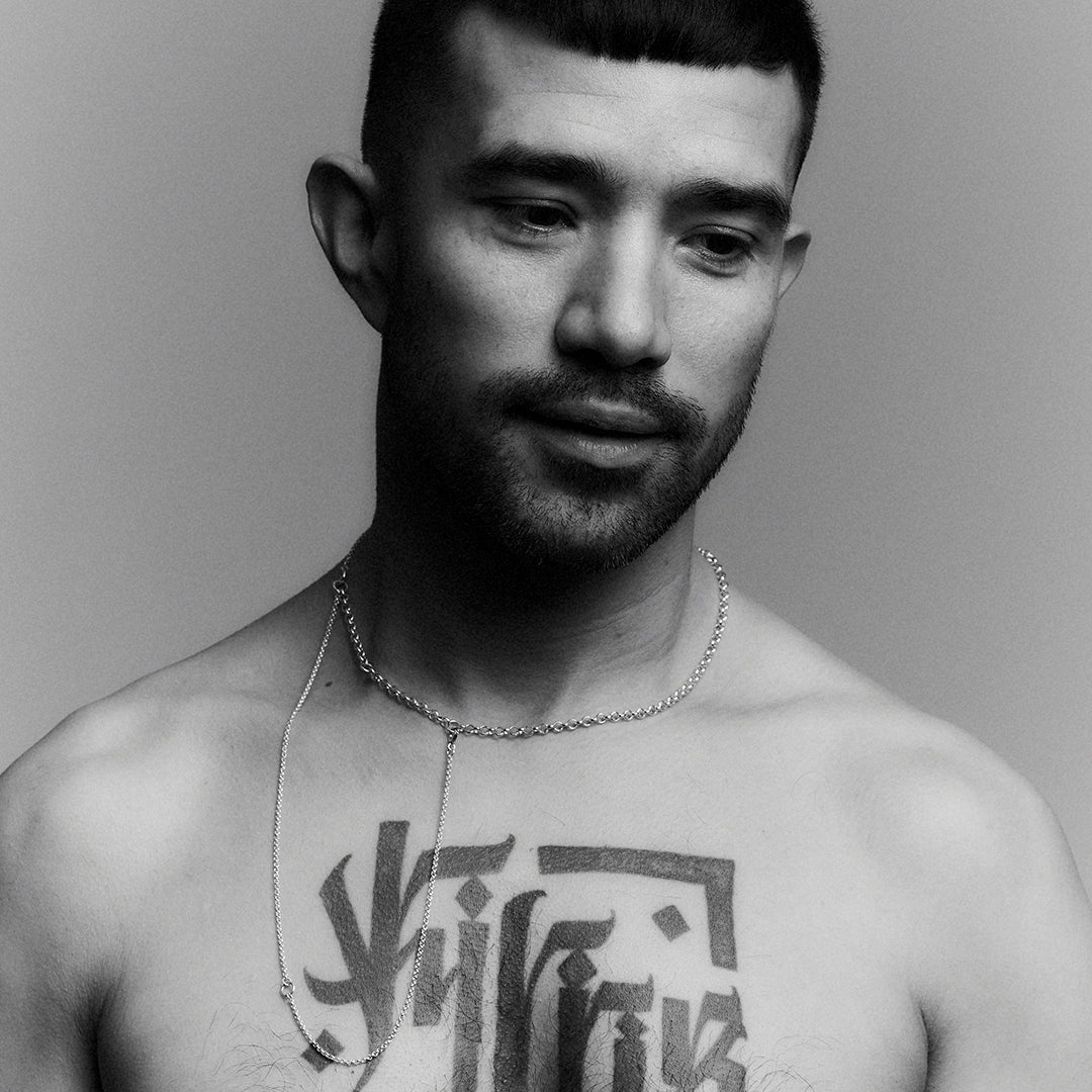 A man's face and neck wearing a double layered silver necklace, with an adjustable clasp.