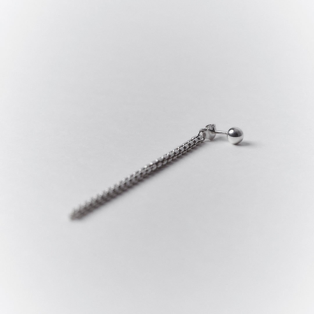 Long dangling silver earring with a ball stud.