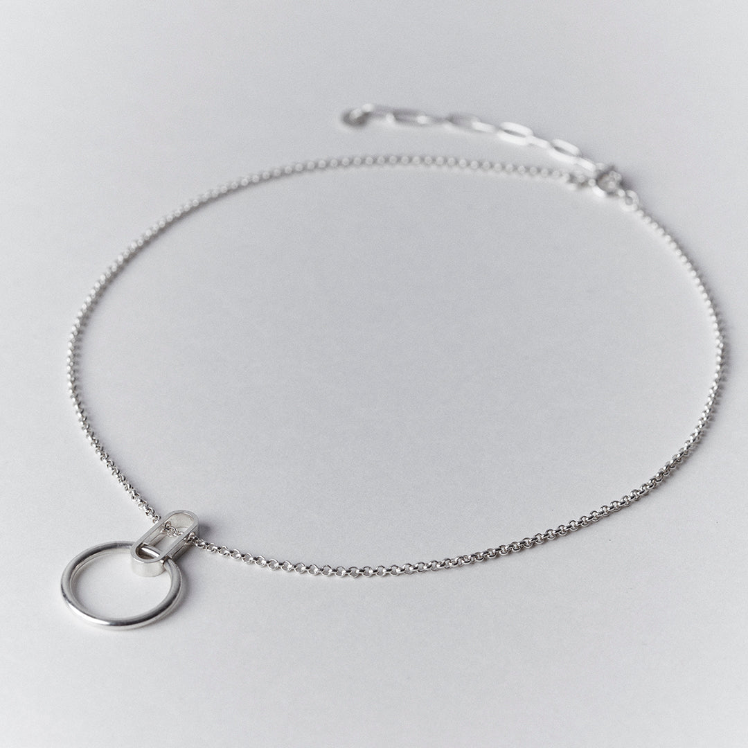 A silver necklace with an oval shape collected to a thick ring.