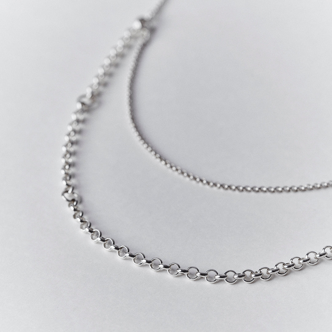 An detailed zoom in photograph of an adjustable silver necklace with a double layered chain.