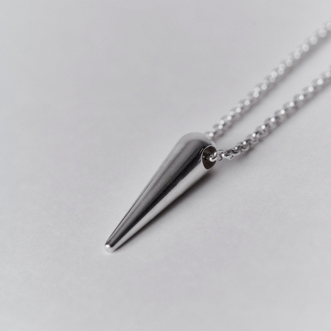 The detail of a silver chain and a silver spike shaped pendant. 