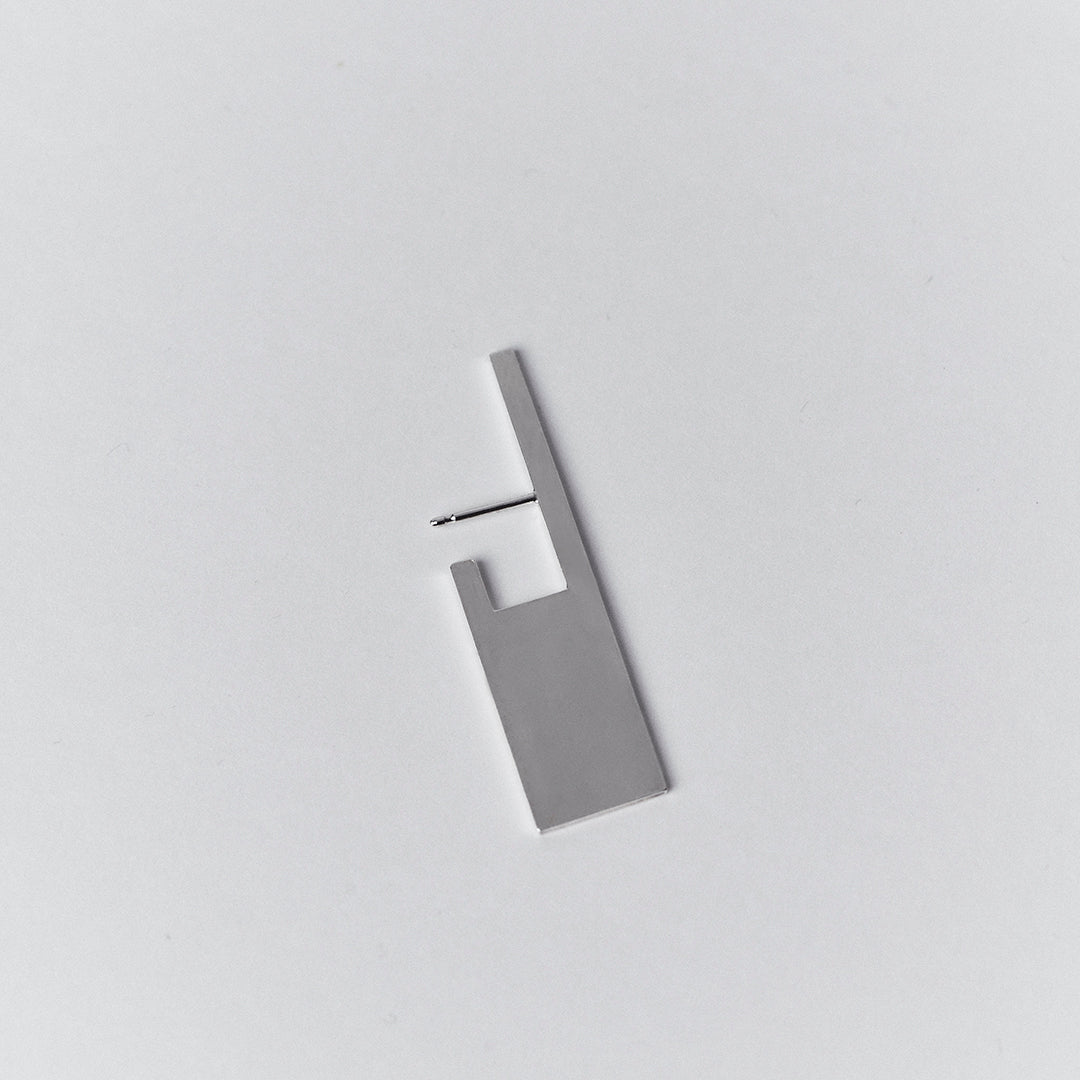 A rectangular shaped silver earring with a cut out that hooks behind the earlobe.