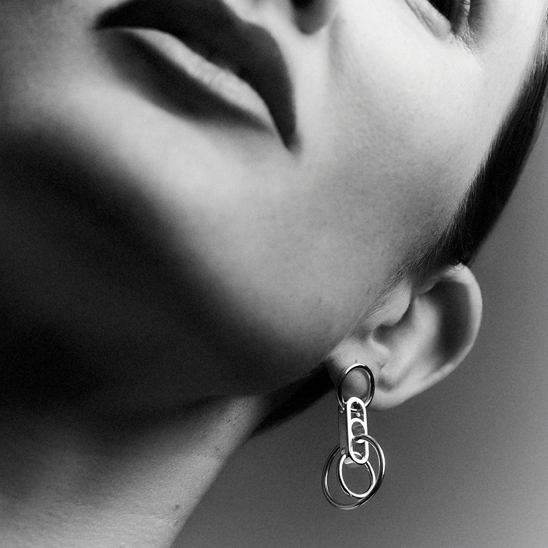 A Woman's partial face shot, showing a silver earring with interlocking silver rings.