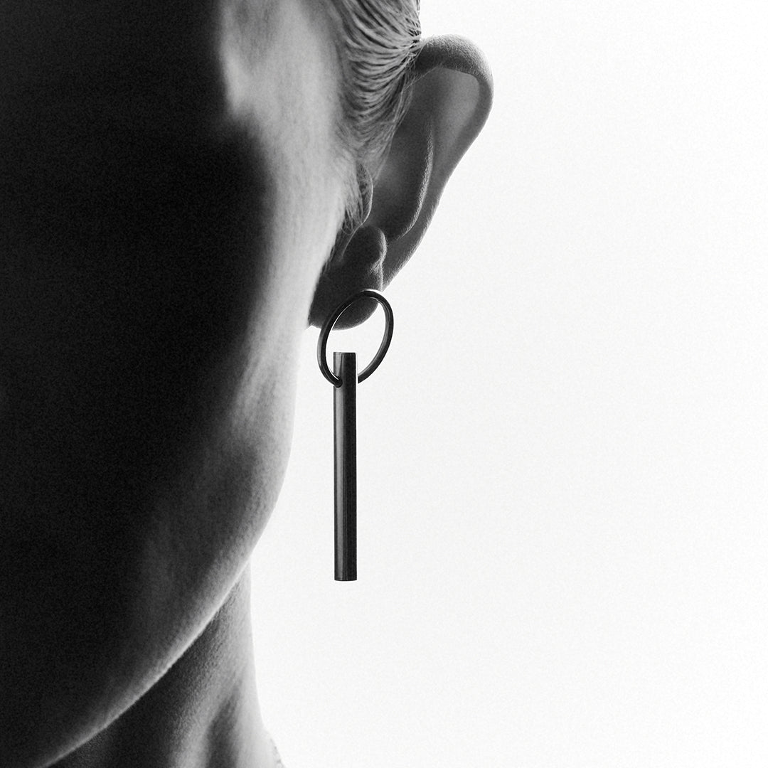 A woman's face in shadow wearing a bold silver earring with a handing bar.