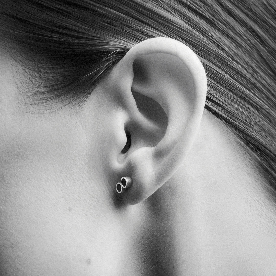 A zoom in of a woman's ear, wearing a silver stud earring with two circles which form an infinity loop.