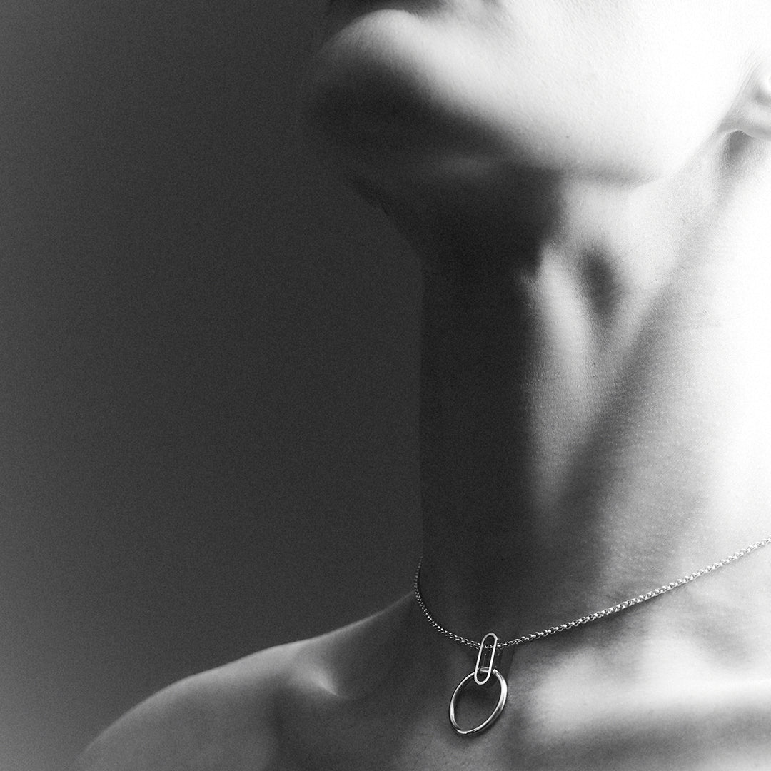 A woman's check and jaw line, wearing a silver choker necklace with an oval shape connected to a ring that rests in between her collar bones. 