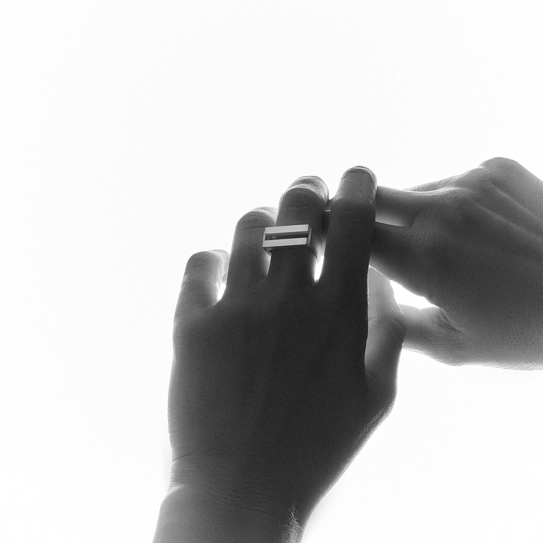 Woman's hands held up to the light wearing a silver ring with parallel bars.