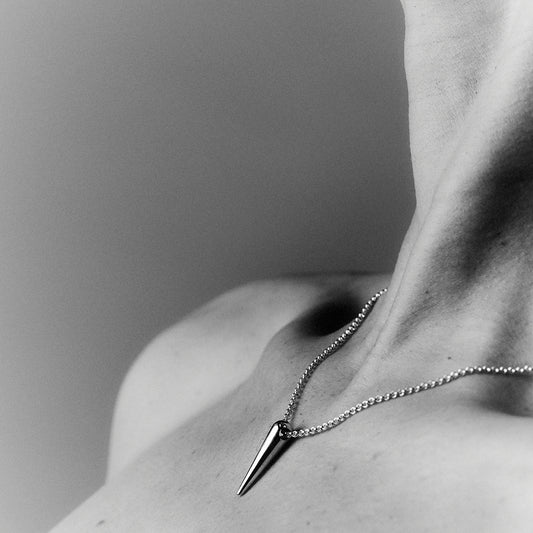 A woman's chest and neck, with a silver chain and a silver spike shaped pendant. 
