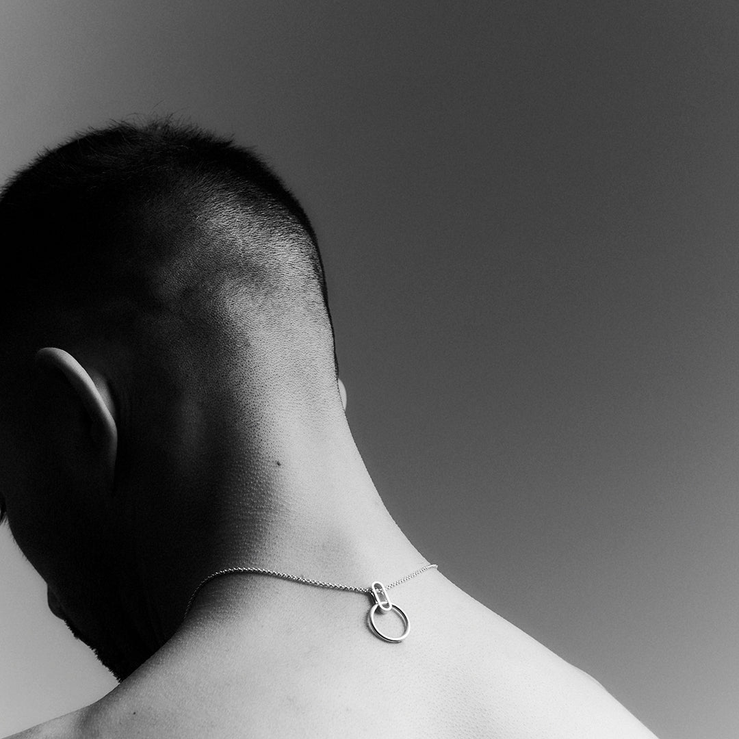 The back of a man's head and neck, wearing a silver necklace backwards.