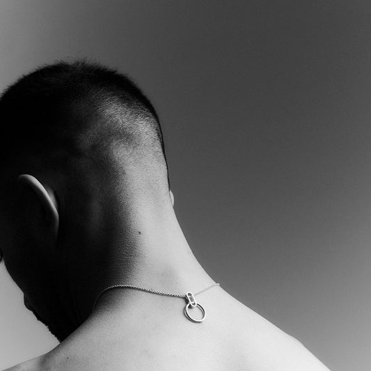 The back of a man's head and neck, wearing a silver necklace backwards.