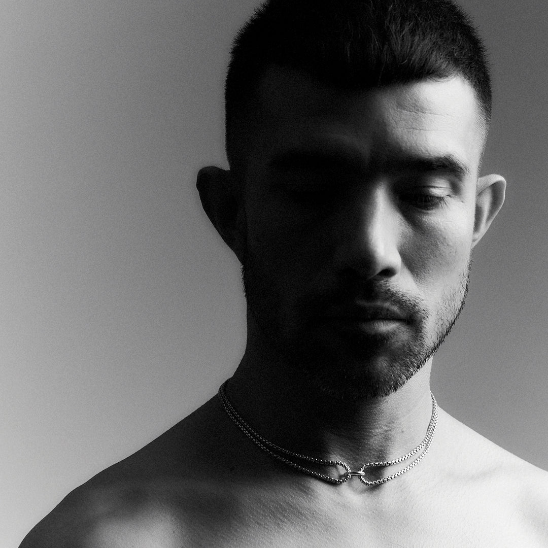 Man wearing a thick silver choker necklace with a double venetian chain and a central ring. 