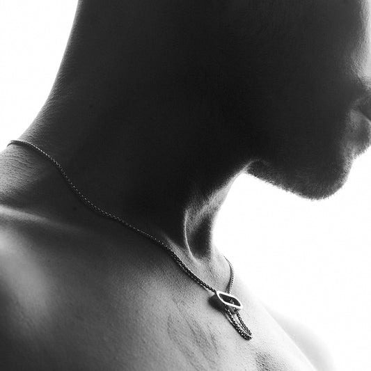 Man's chest wearing a silver necklace with an oval pendant and a thick venetian chain.