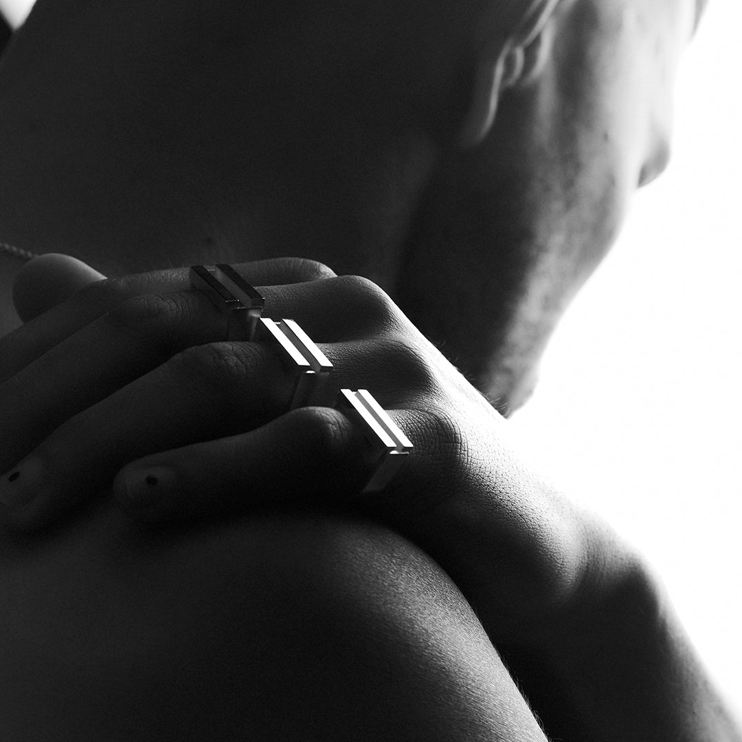 Man's hand on his shoulder, wearing three silver rings with parallel bars on his fingers. 