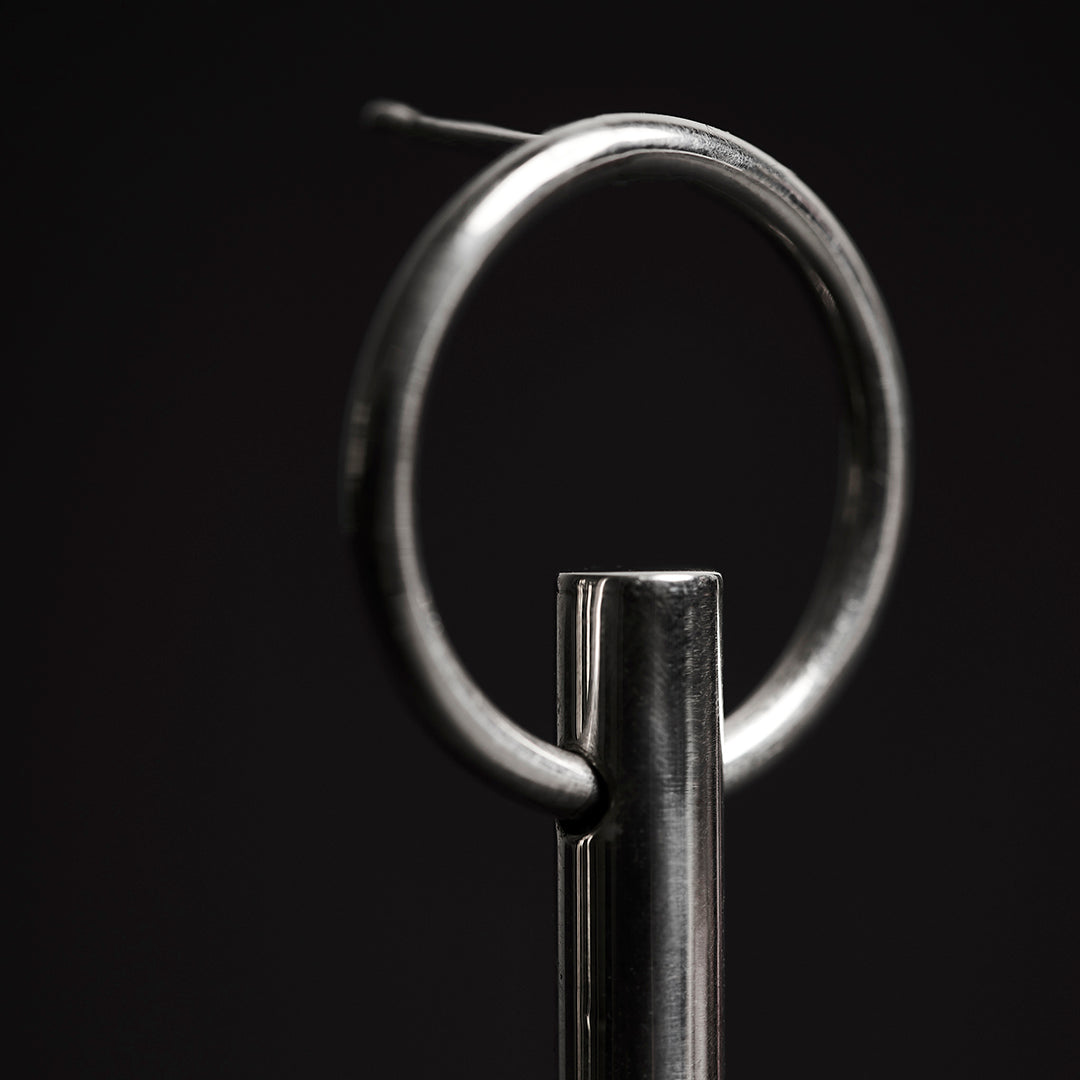 Zoom in of a a bold silver earring with a thick bar handing on a ring.