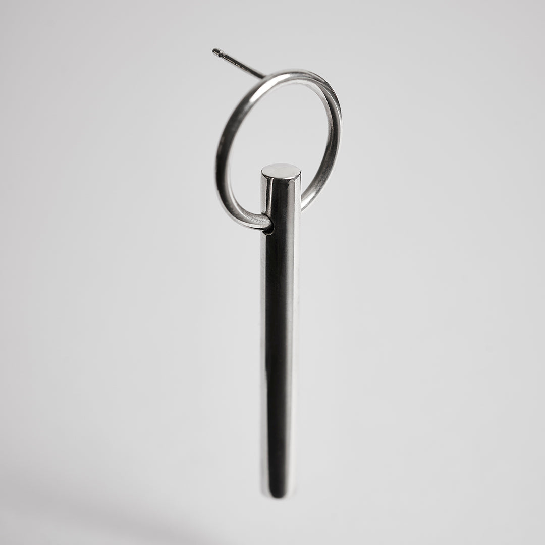 A bold silver earring with a thick bar handing on a ring.